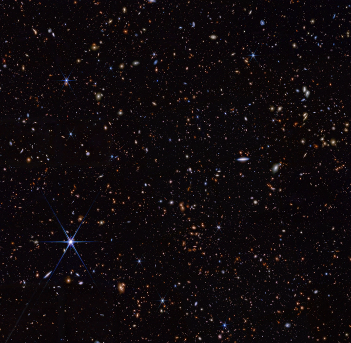 This infrared image from NASA’s James Webb Space Telescope (also called Webb or JWST) was taken by the NIRCam (Near-Infrared Camera) for the JWST Advanced Deep Extragalactic Survey, or JADES, program. The NIRCam data was used to determine which galaxies to study further with spectroscopic observations. In the background image, blue represents light at 0.90, 1.15, and 1.50 microns (filters F090W + F115W + F150W), green is 2.00 and 2.77 microns (F200W + F277W), and red is 3.56, 4.10, and 4.44 microns (F356W + F410M + F444W). The pullout image shows light at 0.90 and 1.15 microns (F090W + F115W) as blue, 1.50 and 2.00 microns (F150W + F200W) as green, and 2.77 microns (F277W) as red.